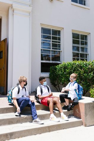 Students sitting outside of school, wearing masks. Photo courtesy of RODNAE Productions.