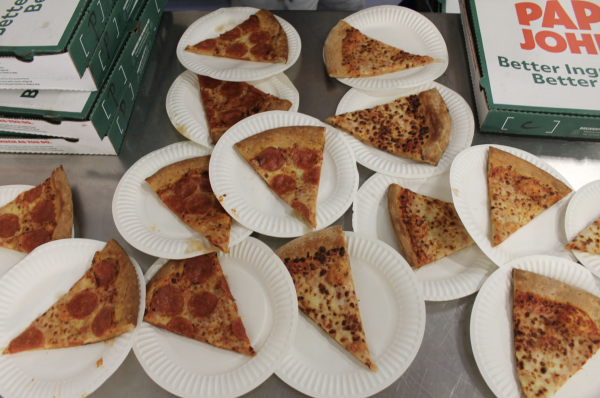 Papa Johns cheese and pepperoni pizza slices on paper plates along with unopened pizza boxes in the school cafeteria.